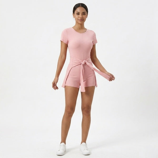 Pink tie-waist romper styled with white sneakers, front view showing the shorts and cape panel.