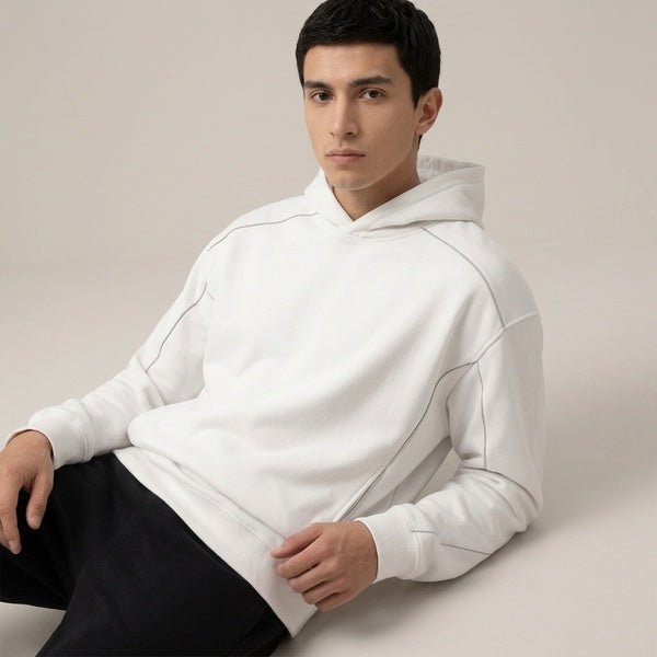 White Unisex Oversized Piping Fleece Hoodie on a seated model, showing the relaxed fit and piping.