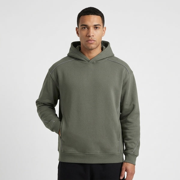 Muted gray-green oversized piping fleece hoodie, model in a front view with hands in the pockets.