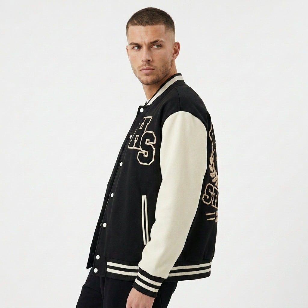 Angled view of the black and cream Two-Tone Fleeced Varsity Jacket with HS lettering and striped cuffs.